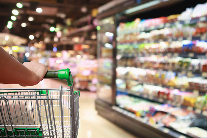 Person holding shopping trolley with food in fridge in the background